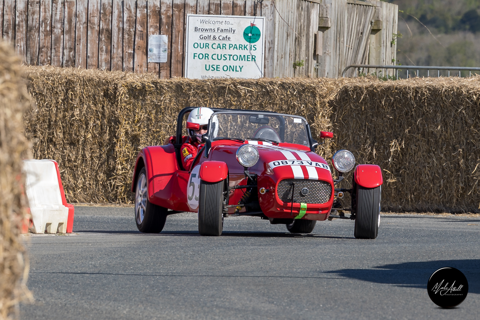 Red Caterham Seven with white stripes attacking the bale-lined course